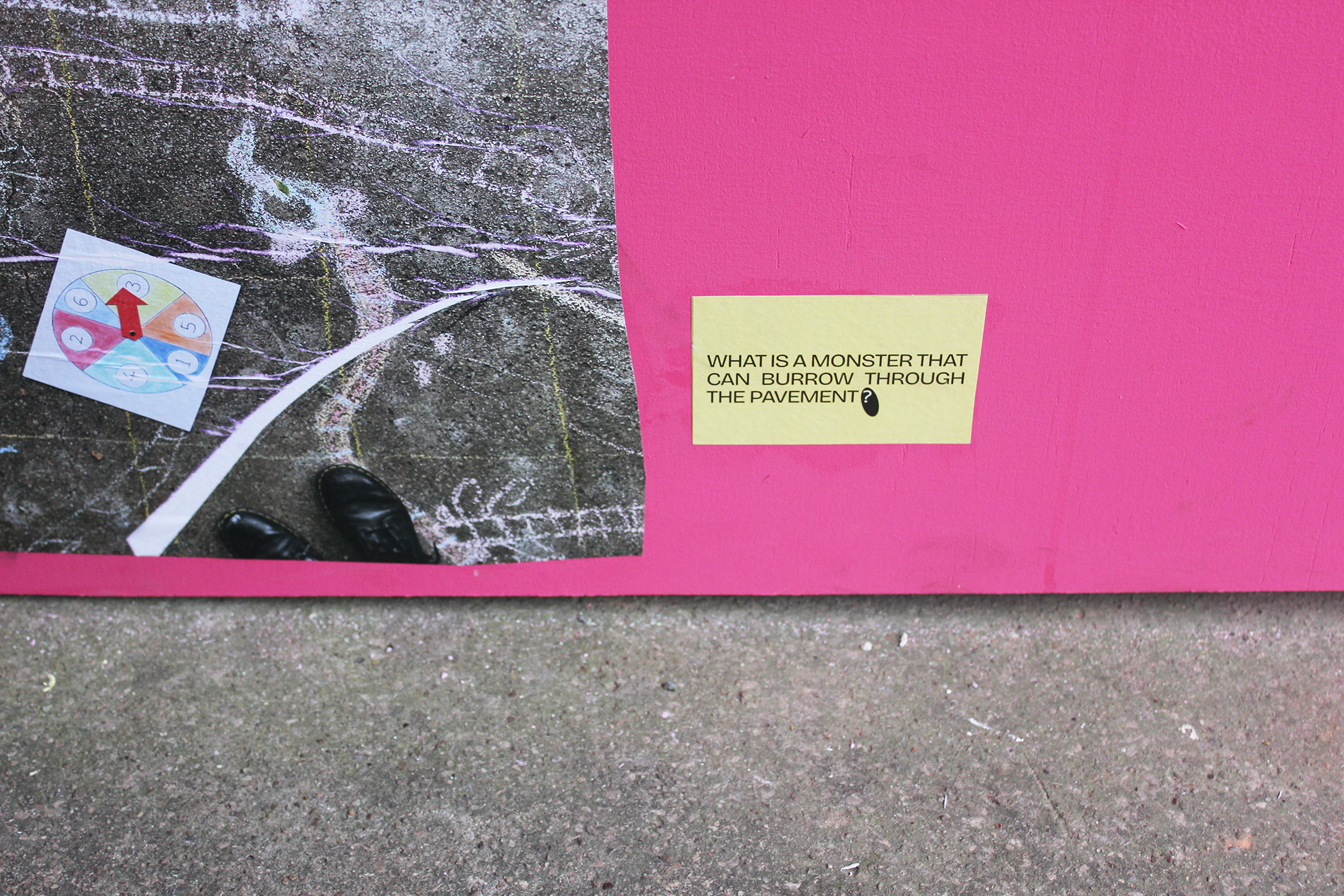 close-up of pink wall meets concrete floor with photo of chalk worms and ladders game and the question 'what is a monster than can burrow through the pavement?'